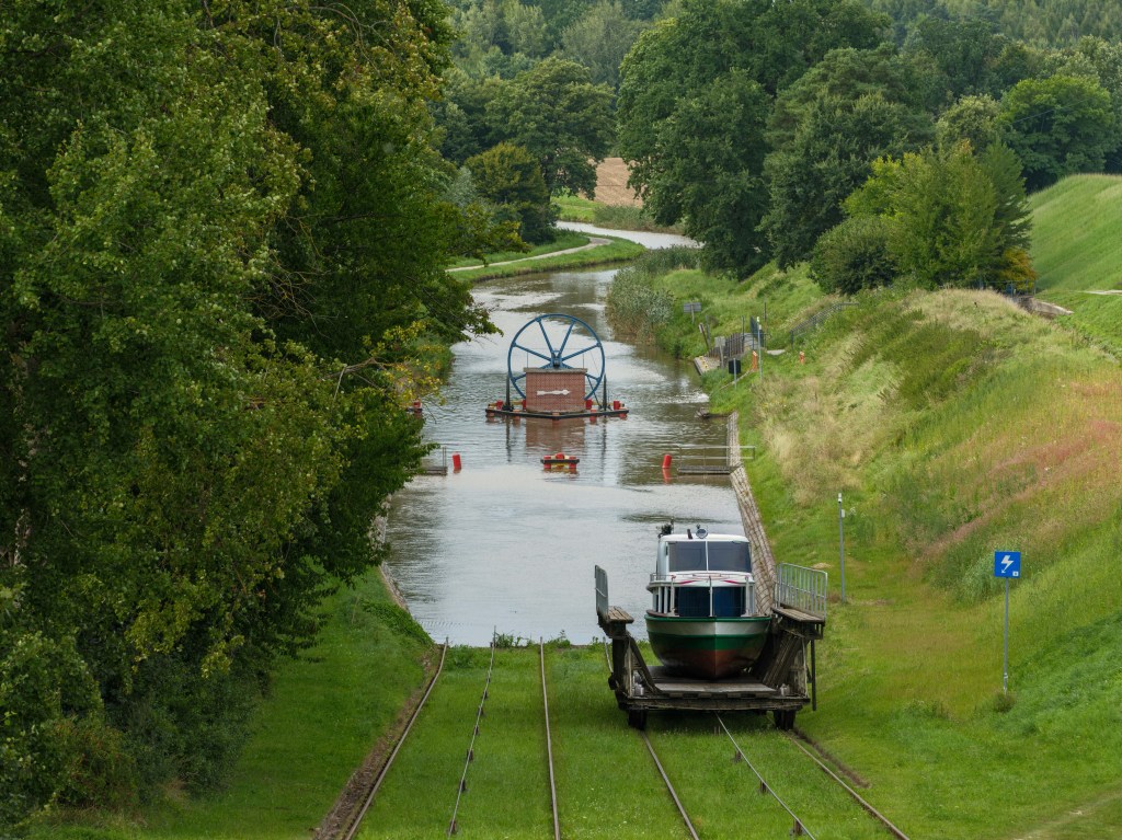 Widok na rzekę z łodzią na torach, otoczoną drzewami na brzegach.